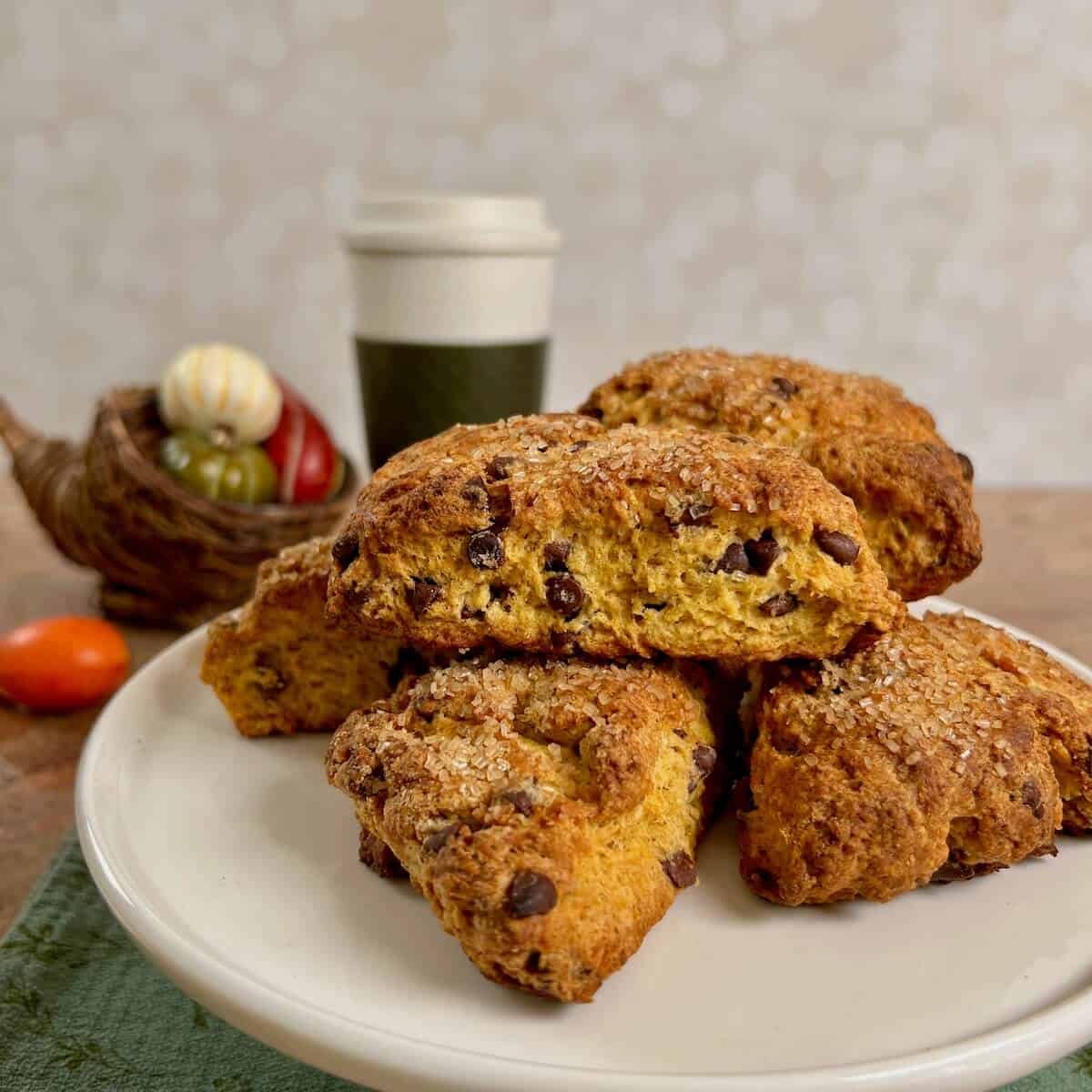 Pumpkin Chocolate Chip Scones stacked on a white cake stand in front of a coffee cup and basket