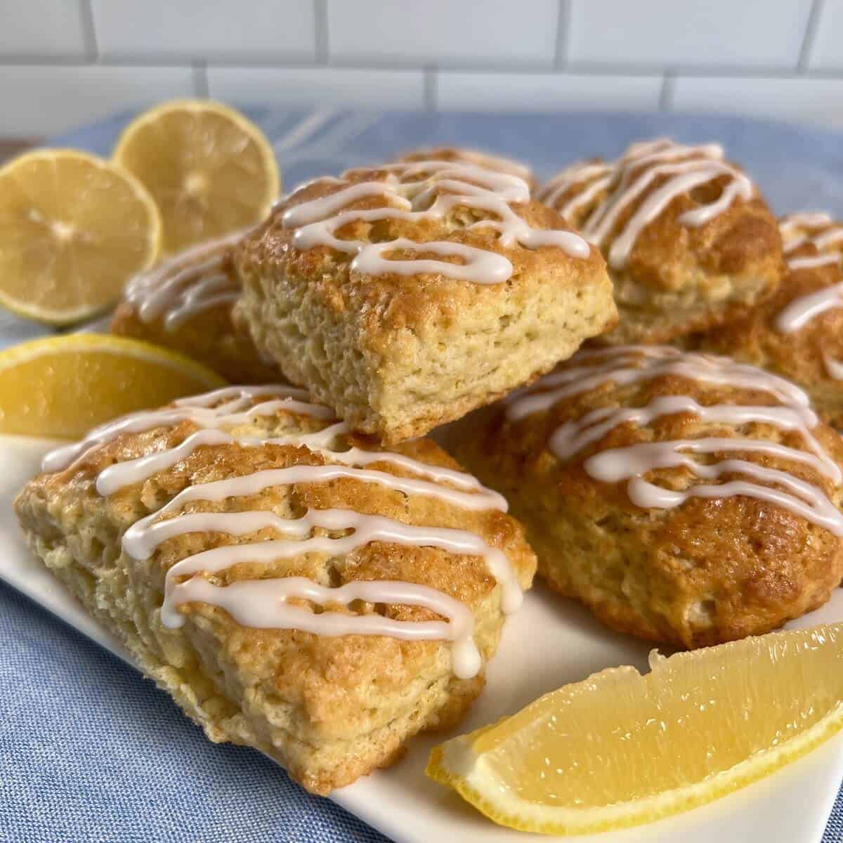 Lemon scones stacked on a white plate with lemon wedges all on a blue towel.