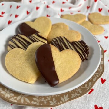 Heart shaped shortbread cutout cookies stacked on a white plate.